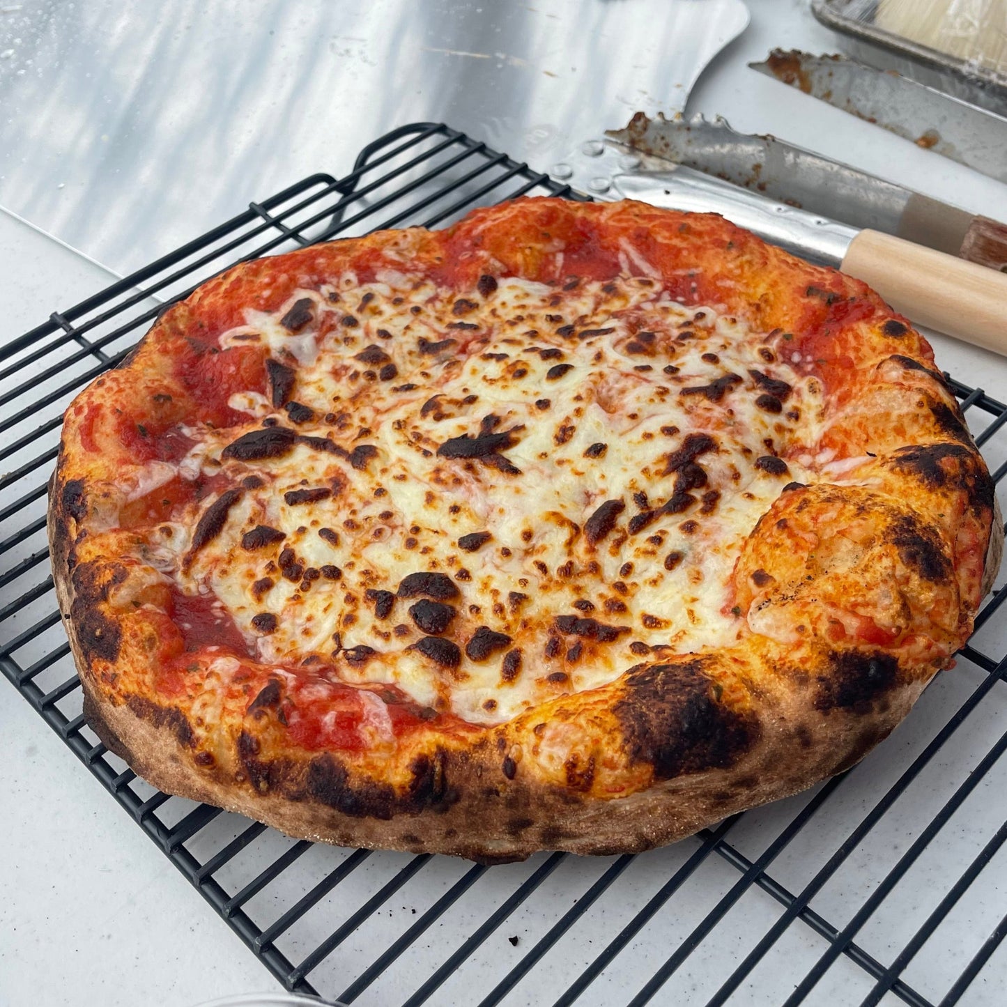 Cheesy pizza on a cooling rack with a spatula nearby